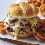 Roast beef sandwich with cheese on a cutting board.