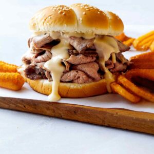 Roast beef sandwich with cheese on a cutting board.