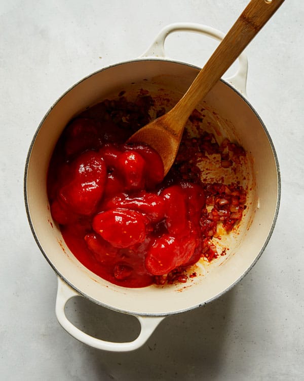 Adding whole tomatoes into a stock pot to make arrabiata sauce.