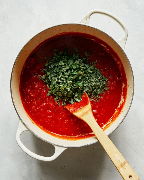 Arrabiata sauce in a stock pot with fresh herbs being added.