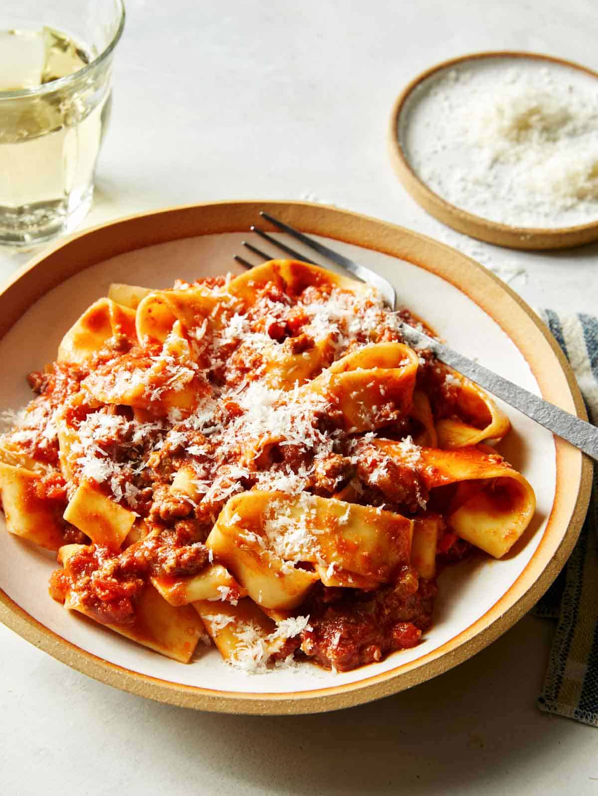 Bolognese sauce with pasta in a bowl with wine in the background.