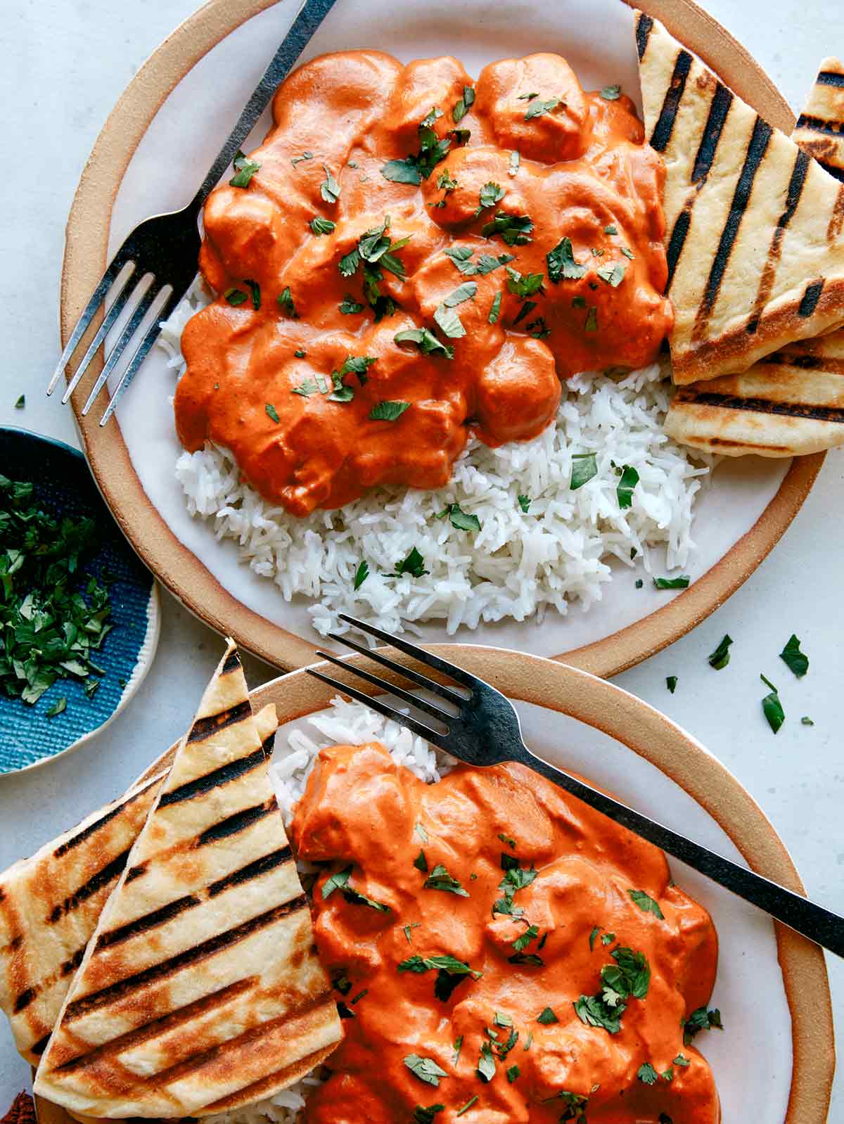 Two servings of butter chicken on plates with bread and rice. 