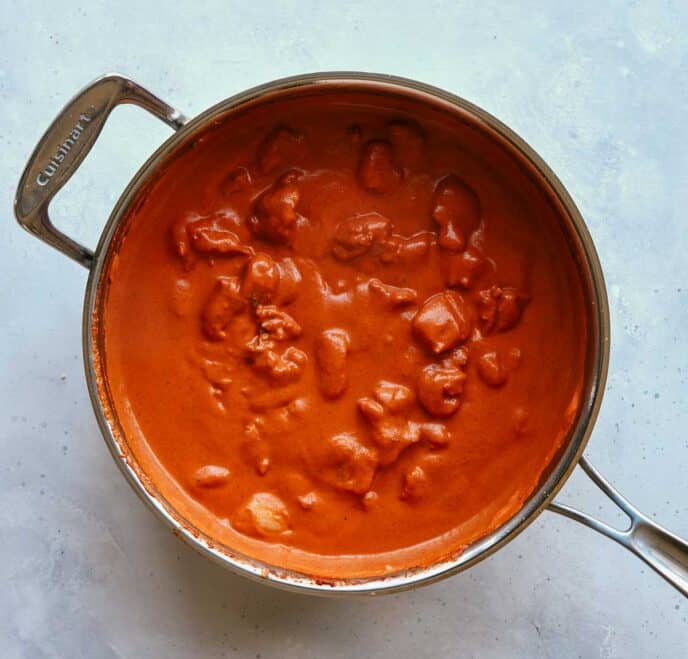 Butter chicken with cream stirred in simmering in a skillet. 