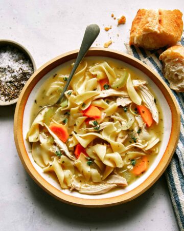 Chicken noodle soup recipe in a bowl with bread on the side.