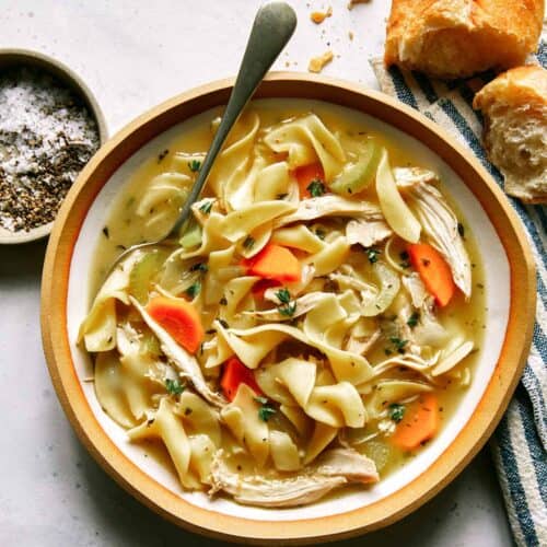 Chicken noodle soup recipe in a bowl with bread on the side.