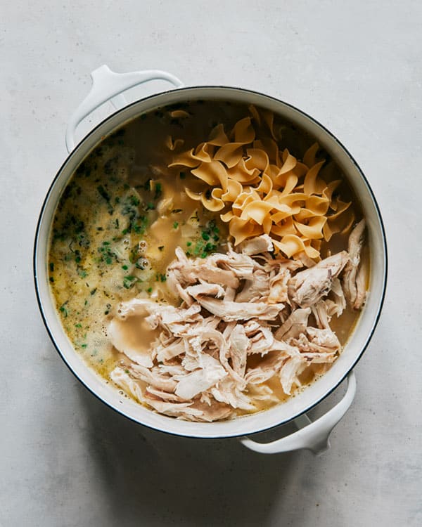 Egg noodles and chicken added to a stock pot for chicken noodle soup. 