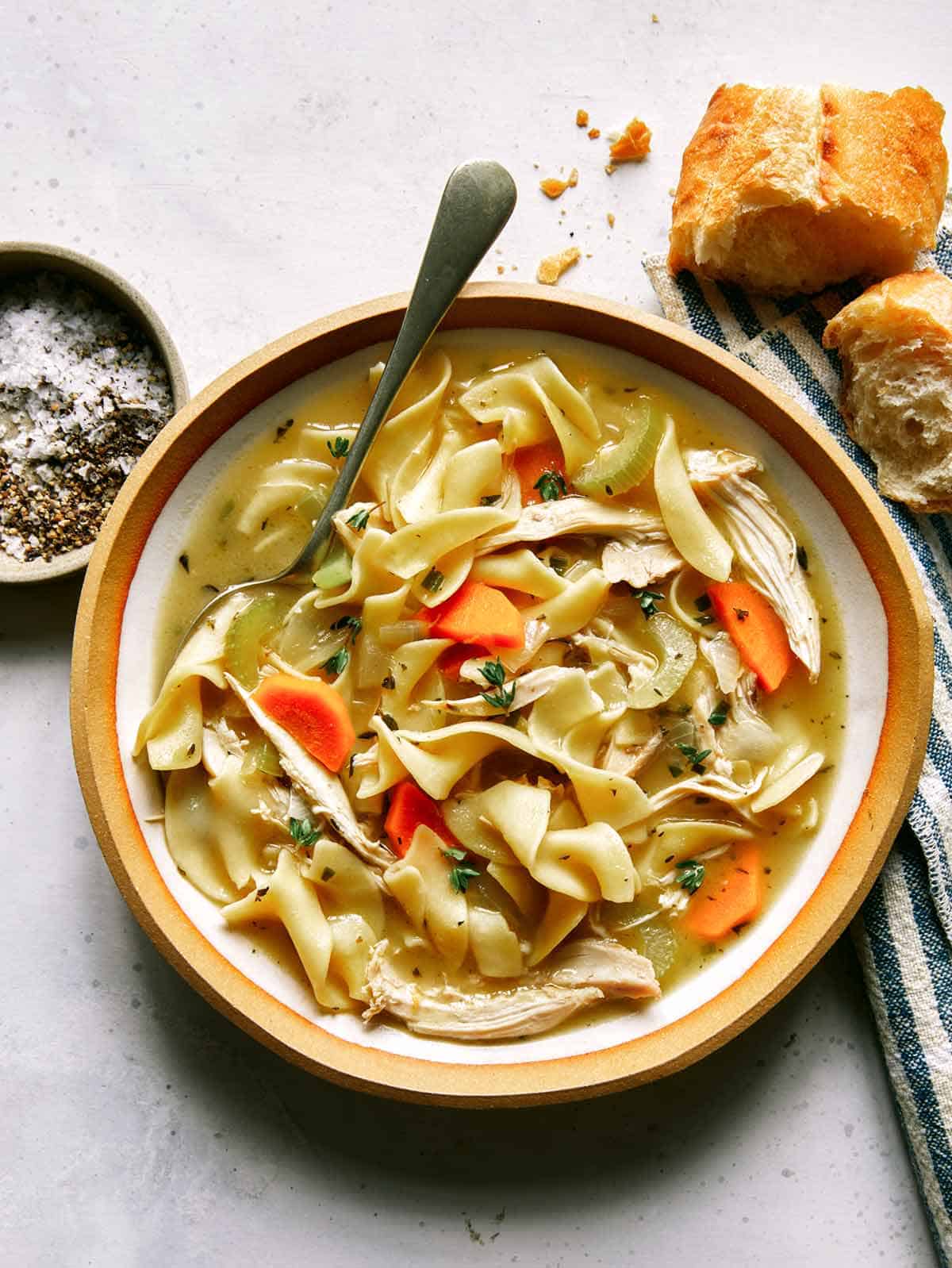 Chicken noodle soup recipe in a bowl with bread on the side. 