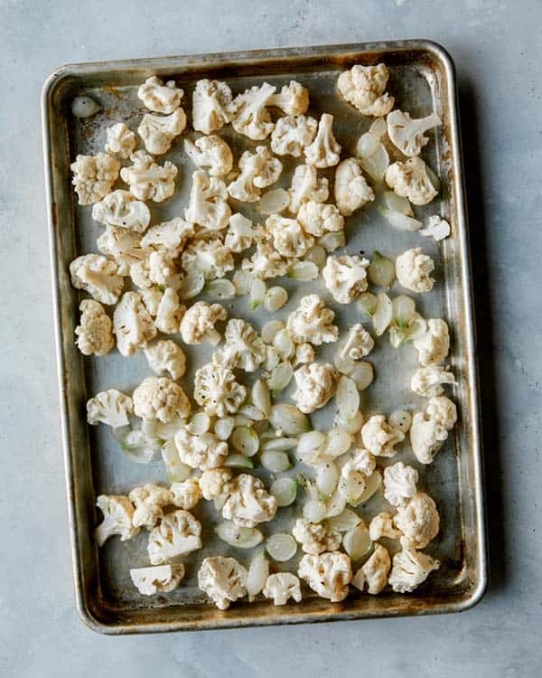 Cauliflower and pearled onions on a baking sheet.