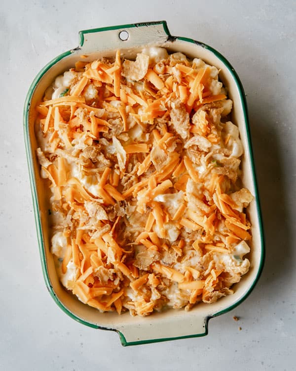 Creamy baked cauliflower topped with cheese and onions to be baked.
