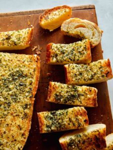 Homemade garlic bread recipe on a cutting board with some cut up.
