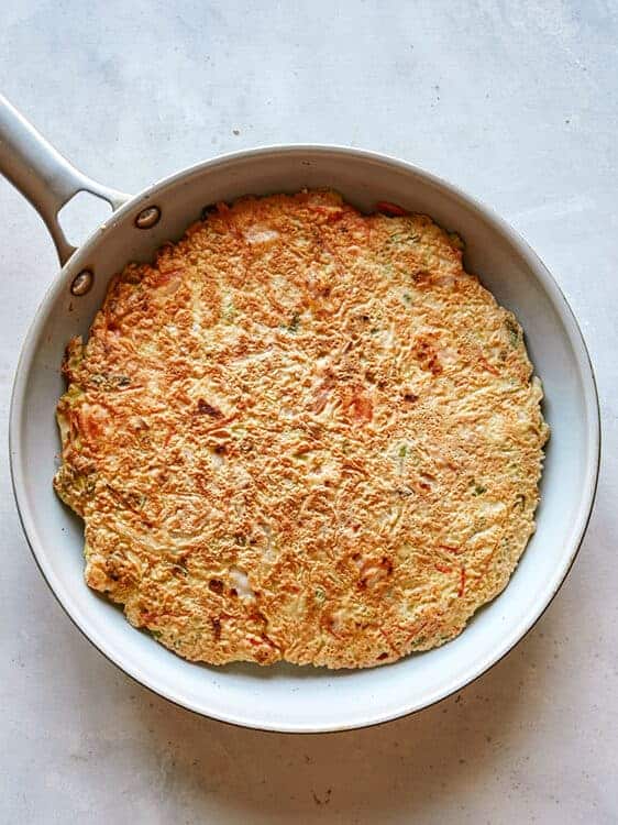 Okonomiyaki cooking in a skillet.