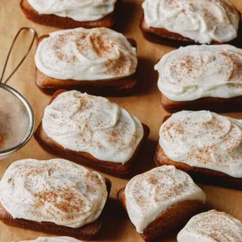 Pumpkin bars with cream cheese frosting on parchment.