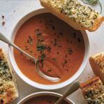 Tomato soup recipe in two bowls with garlic bread on the side.