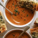 Tomato soup recipe in two bowls with garlic bread on the side.