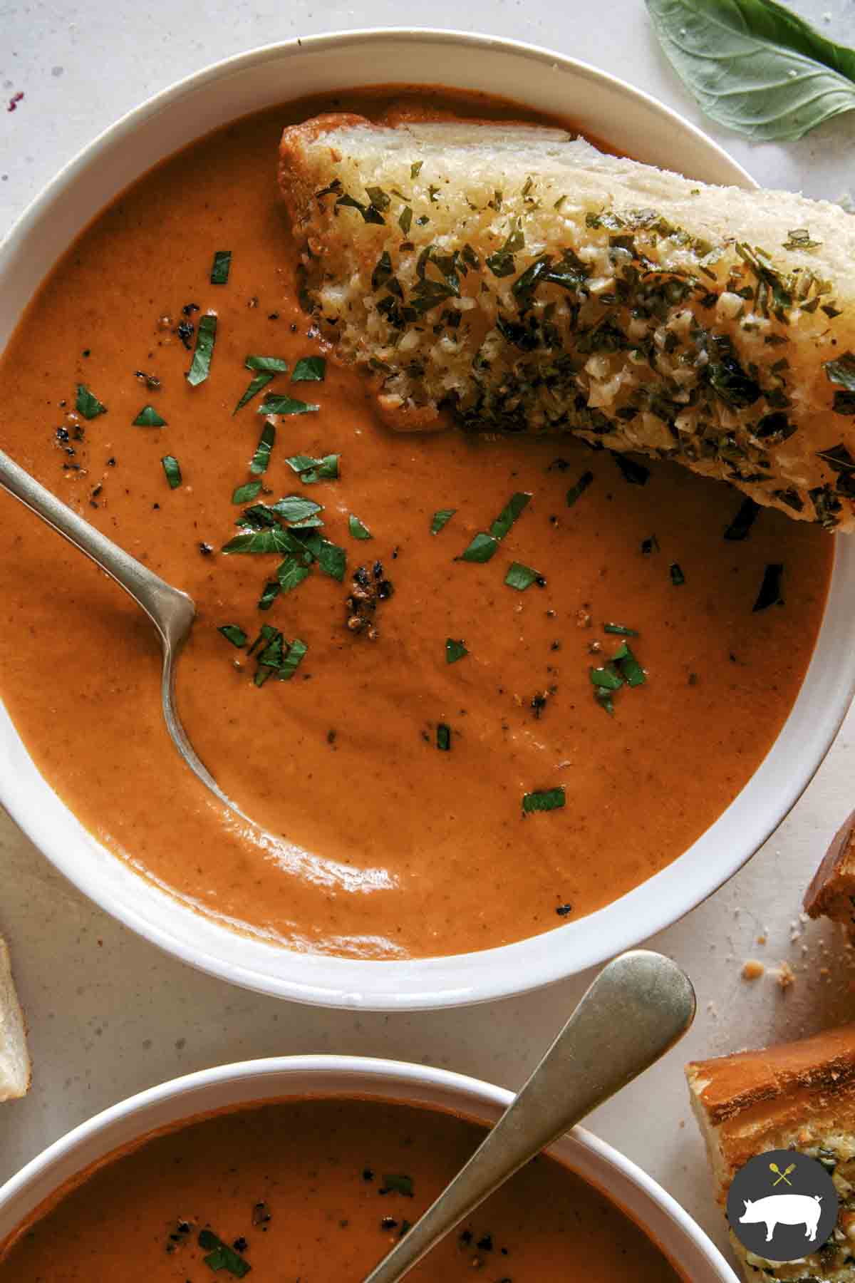 Tomato soup recipe in two bowls with garlic bread on the side.