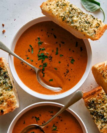 Tomato soup recipe in two bowls with garlic bread on the side.