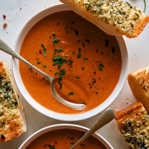 Tomato soup recipe in two bowls with garlic bread on the side.