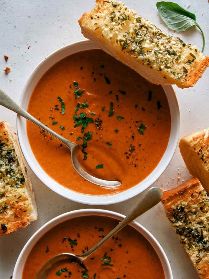 Tomato soup recipe in two bowls with garlic bread on the side.