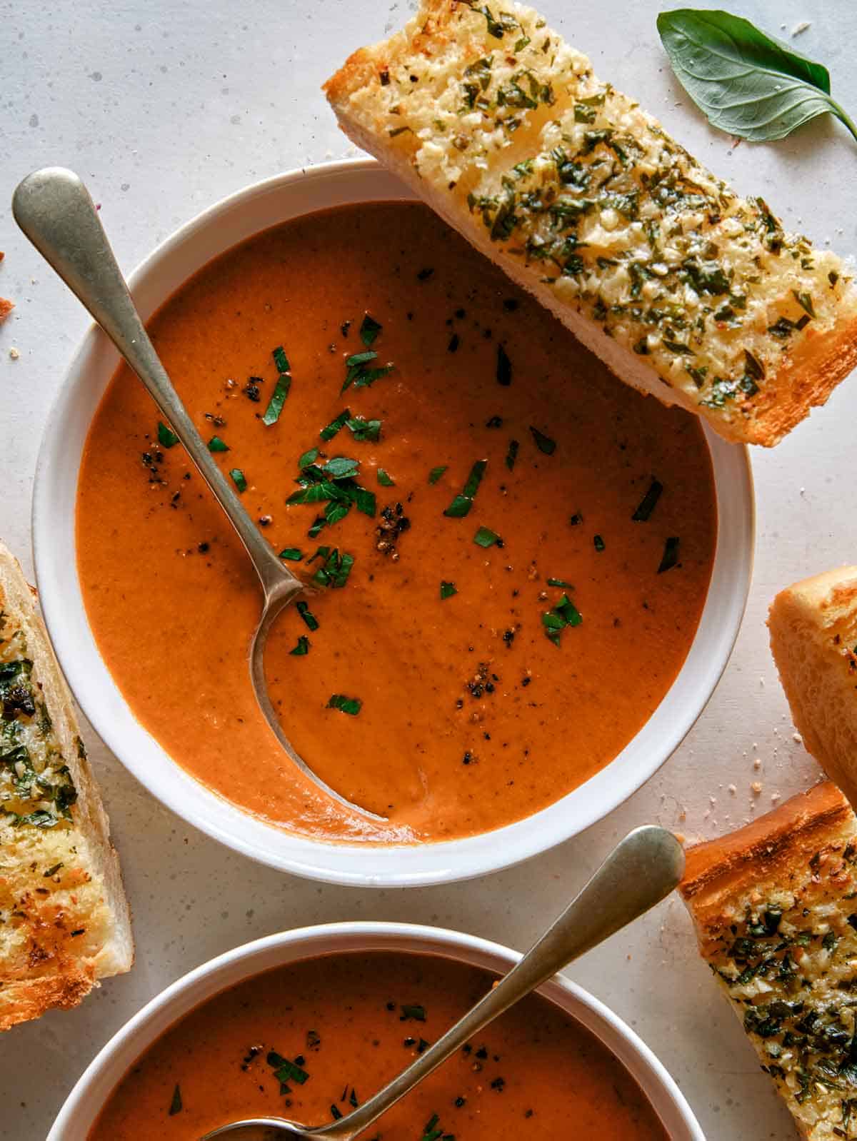 Tomato soup recipe in two bowls with garlic bread. 