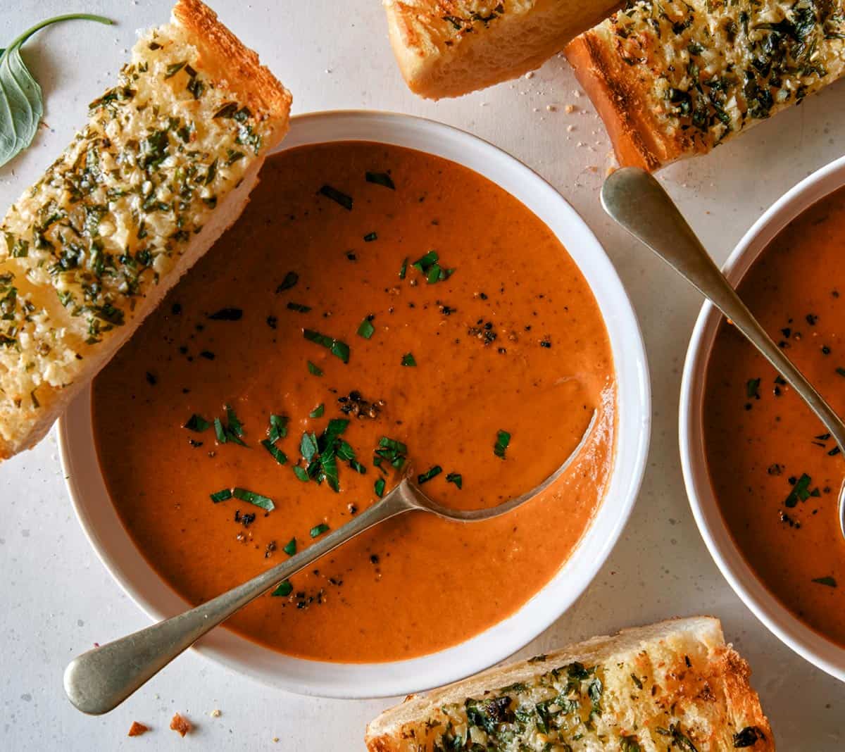 Tomato soup recipe in two bowls with garlic bread on the side.