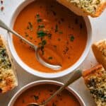 Tomato soup recipe in two bowls with garlic bread on the side.