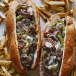 Two Philly Cheesesteak sandwiches with french fries.