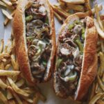 Two Philly Cheesesteak sandwiches with french fries.