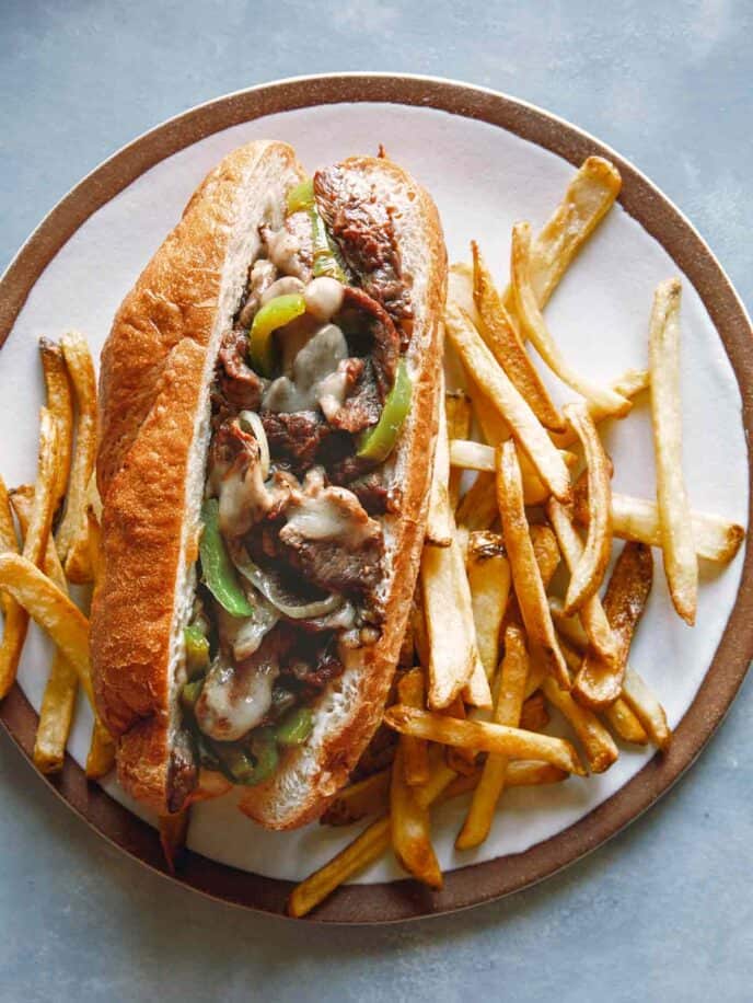 Philly cheesesteak sandwich on a plate with french fries. 