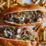 Two Philly Cheesesteak sandwiches with french fries.