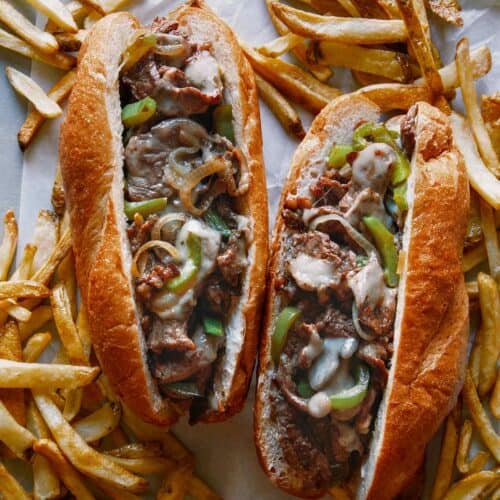 Two Philly Cheesesteak sandwiches with french fries.