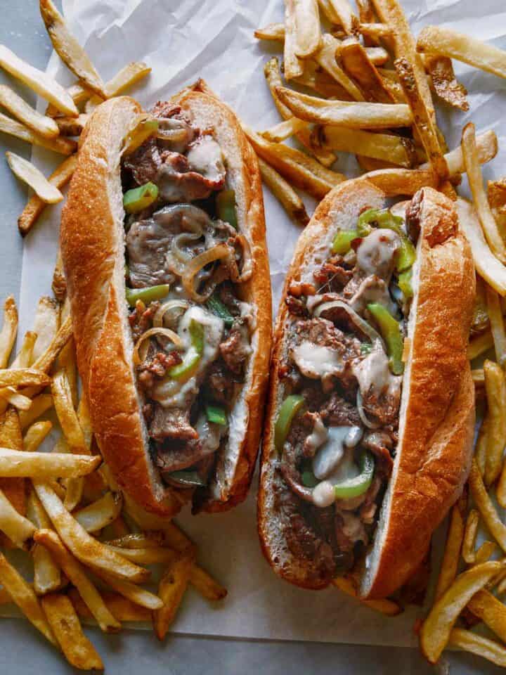 Two Philly Cheesesteak sandwiches with french fries.