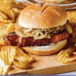 Pork chop sandwiches on a cutting board with potato chips.