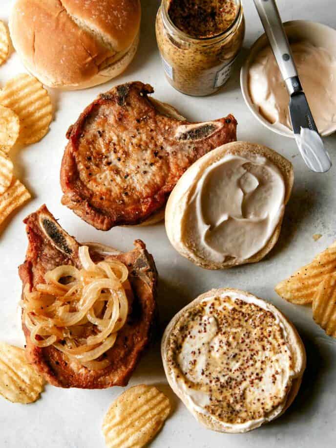 Assembling pork chop sandwiches with potato chips on the side. 