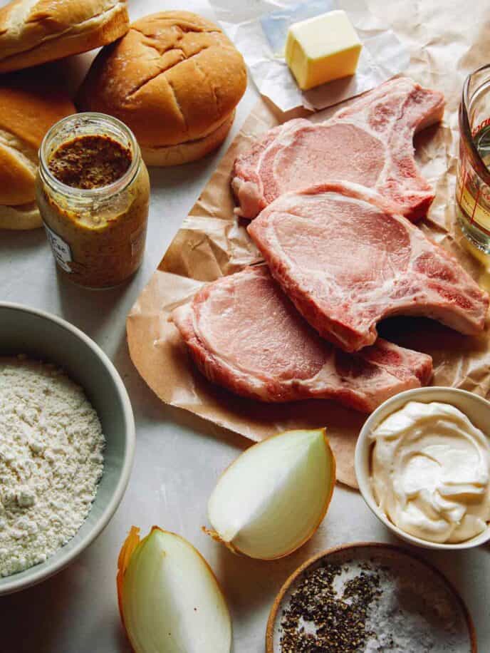 Ingredients to make pork chop sandwiches laid out on a kitchen counter. 