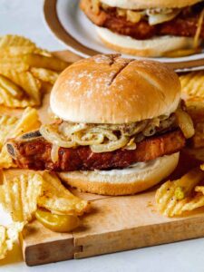 Pork chop sandwiches on a cutting board served with potato chips.