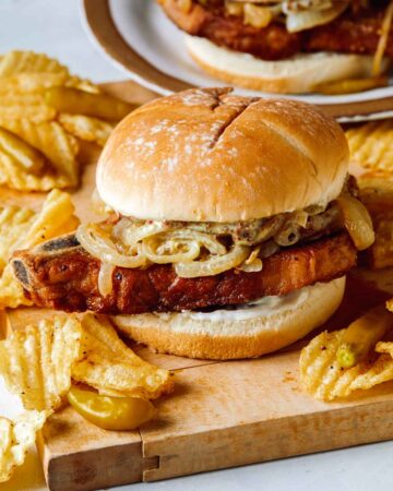 Pork chop sandwiches on a cutting board served with potato chips.