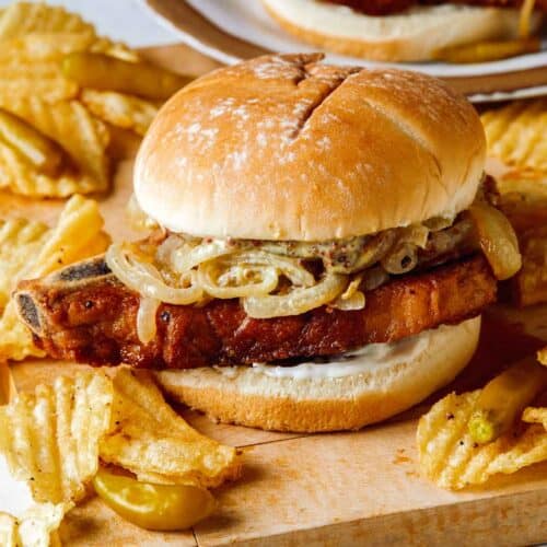 Pork chop sandwiches on a cutting board served with potato chips.