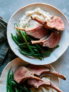 Roasted rack of lamb on a plate with green beans and mashed potatoes.