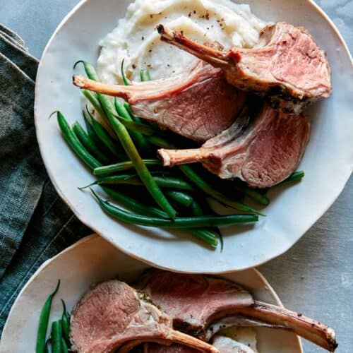 Roasted rack of lamb on a plate with green beans and mashed potatoes.