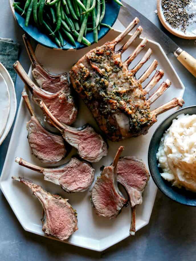 Rack of lamb on a platter with green beans and mashed potatoes.