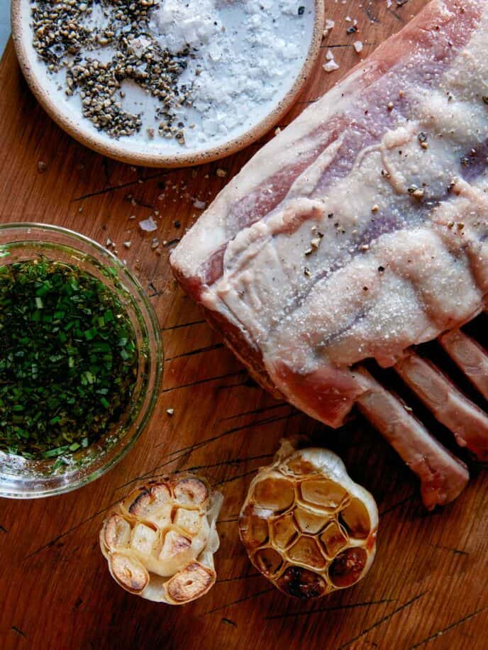 Seasoned rack of lamb with roasted garlic next to it. 