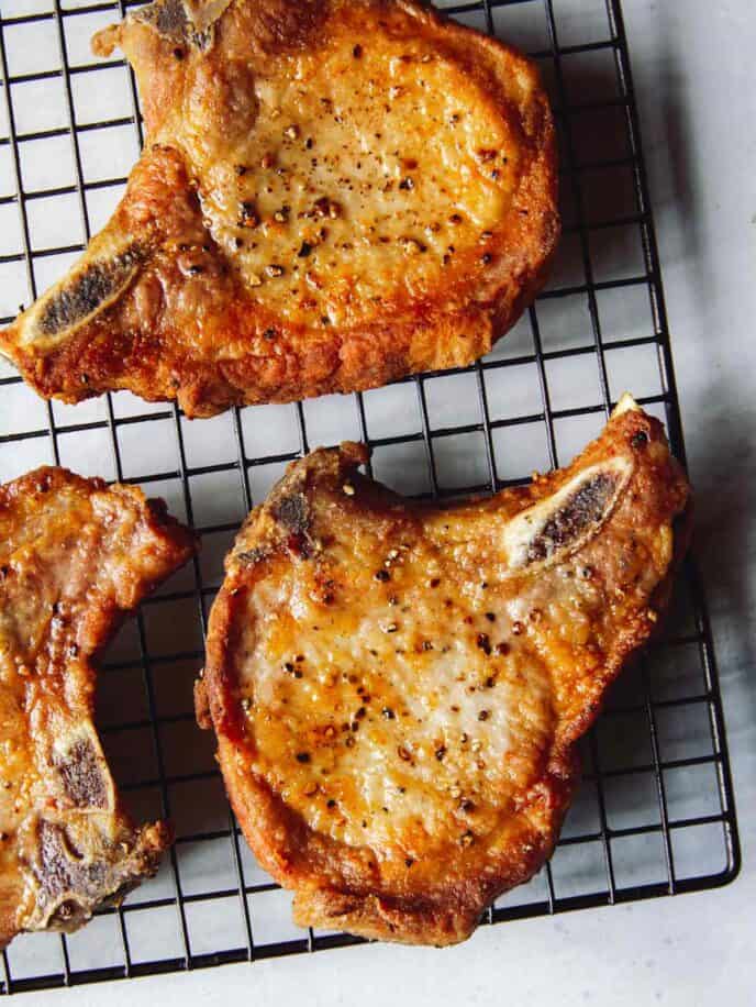 Seared pork chops resting on a baking rack.