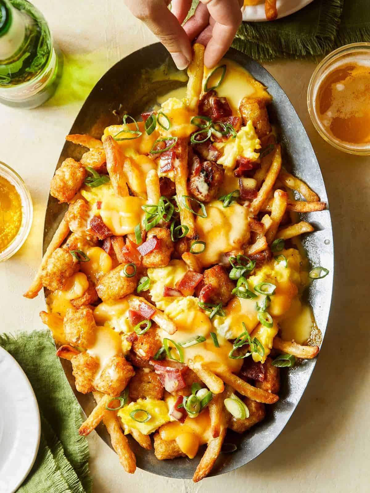 A plate of breakfast poutine with hollandaise sauce and drinks.