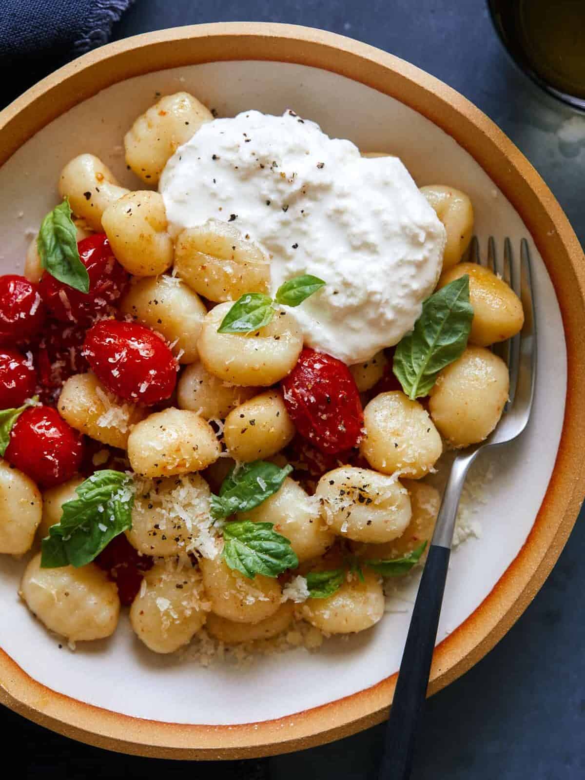 A close up of a bowl of caprese gnocchi and a fork.
