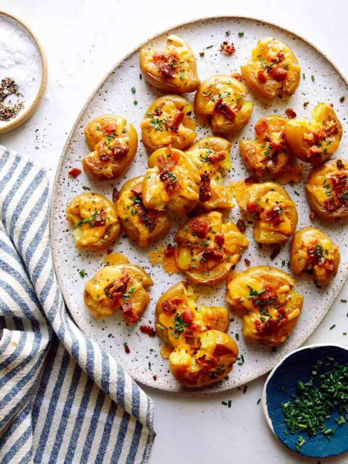 Smashed potatoes recipe on a platter with chives on the side.