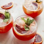 Three blood orange shandy cocktails with slices of oranges on the side.