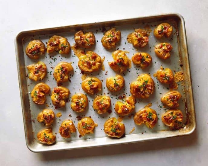 Smashed potatoes on a baking sheet topped with chives.