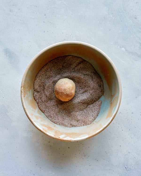 Snickerdoodle dough being rolled in cinnamon sugar.