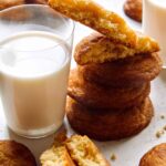 Snickerdoodle cookies stacked next to a glass of milk.