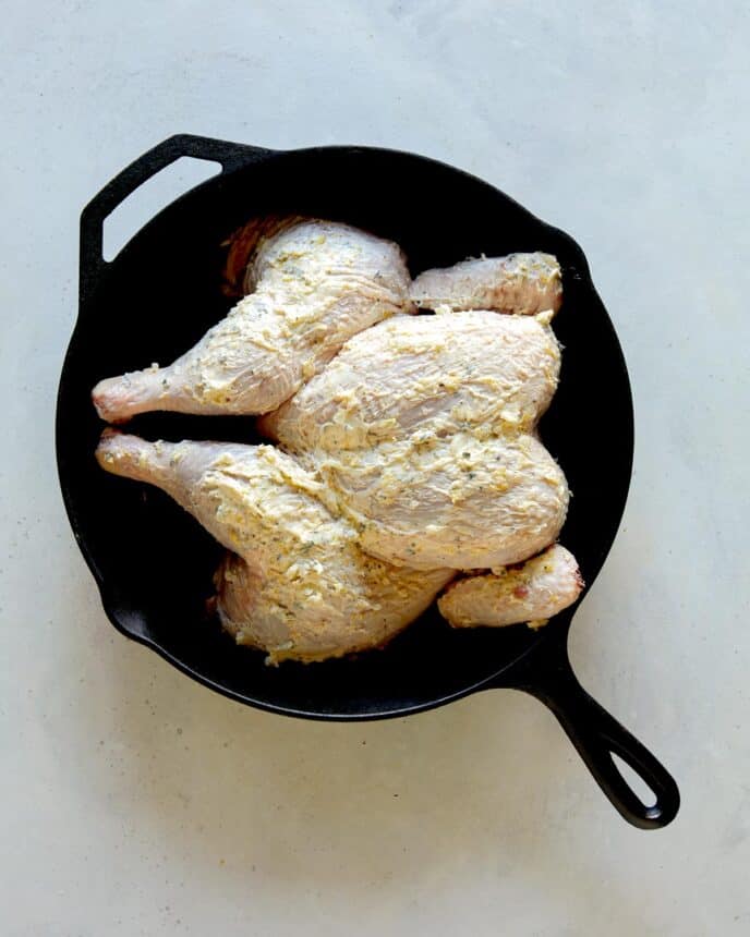 A spatchcock chicken covered in butter in a skillet.